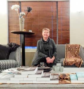 Ruth sits at a table of which are spread copies of her new novel The Tin Heart Gold Mine