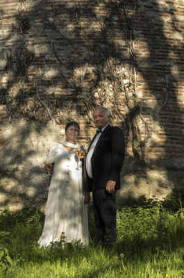 A man and woman holding champagne glasses stand in front of a tower with a tree shadow on it