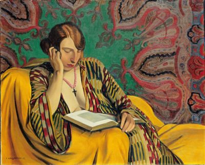 A woman in a Turkish dressing-gown reads a book sitting on  a chair draped in a yellow cloth in front of an exotic wall hanging