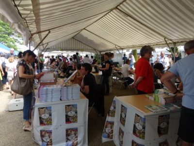 People reading books displayed on tables by the authors under a marquee 