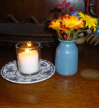 The photo shows a lit memorial candle and a few flowers in a small vase.