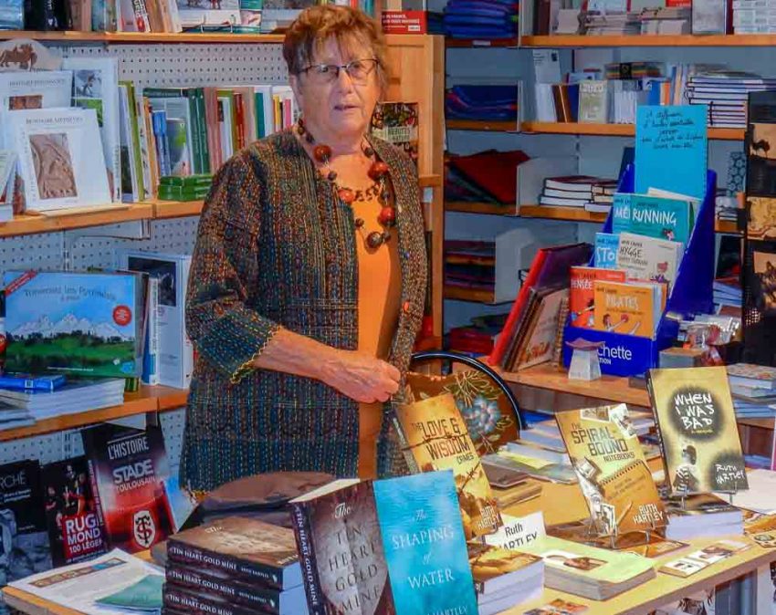 Standing behind a table displaying all her books, Ruth explains the background that substantiates her claim to have taken a lifetime to write the three books launched at La Litote