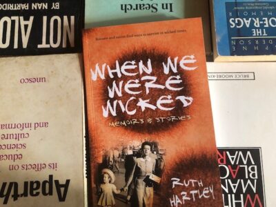 Photo of the book "When We Were Wicked" by Ruth Hartley, lying over five other books which are upside down in relation to Ruth's book, with their titles all partially obscured.